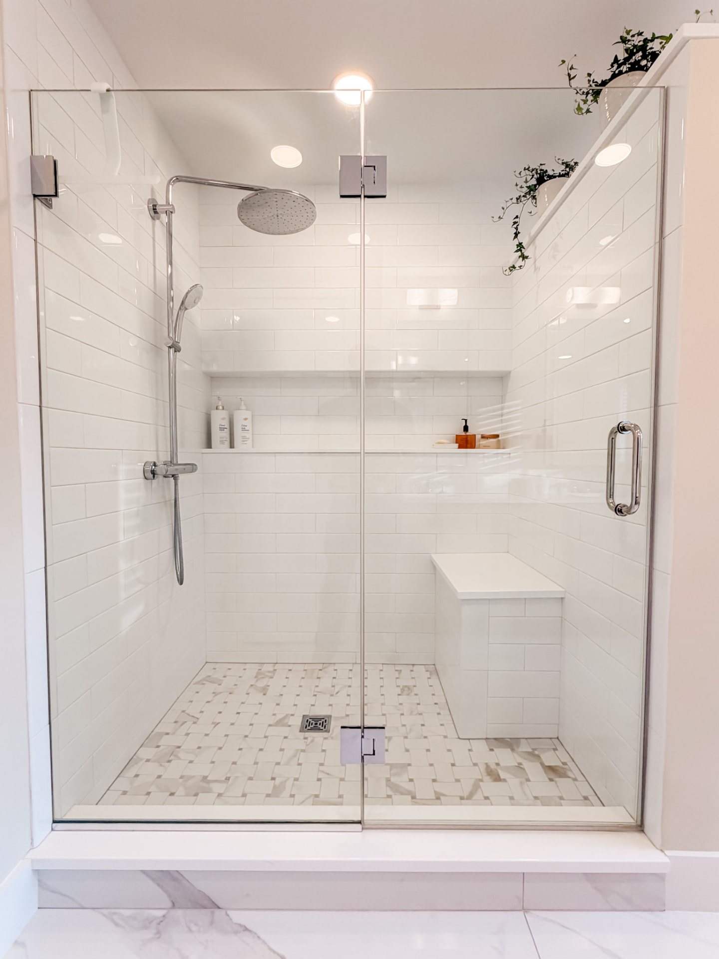 Frameless glass shower with white subway tile, rainfall showerhead, handheld fixture, recessed shelf, and built-in bench