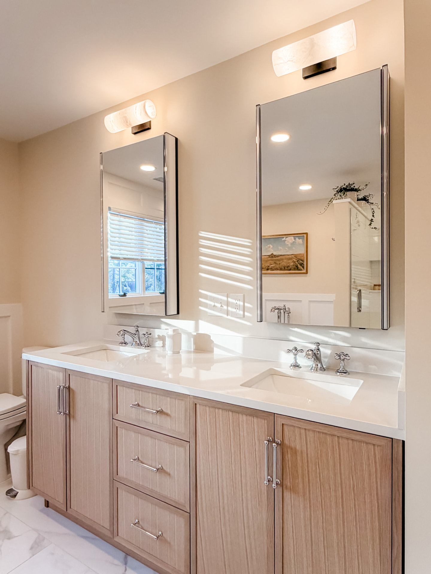 Custom light oak double vanity with white countertop, polished fixtures, matching mirrors, and modern wall lights