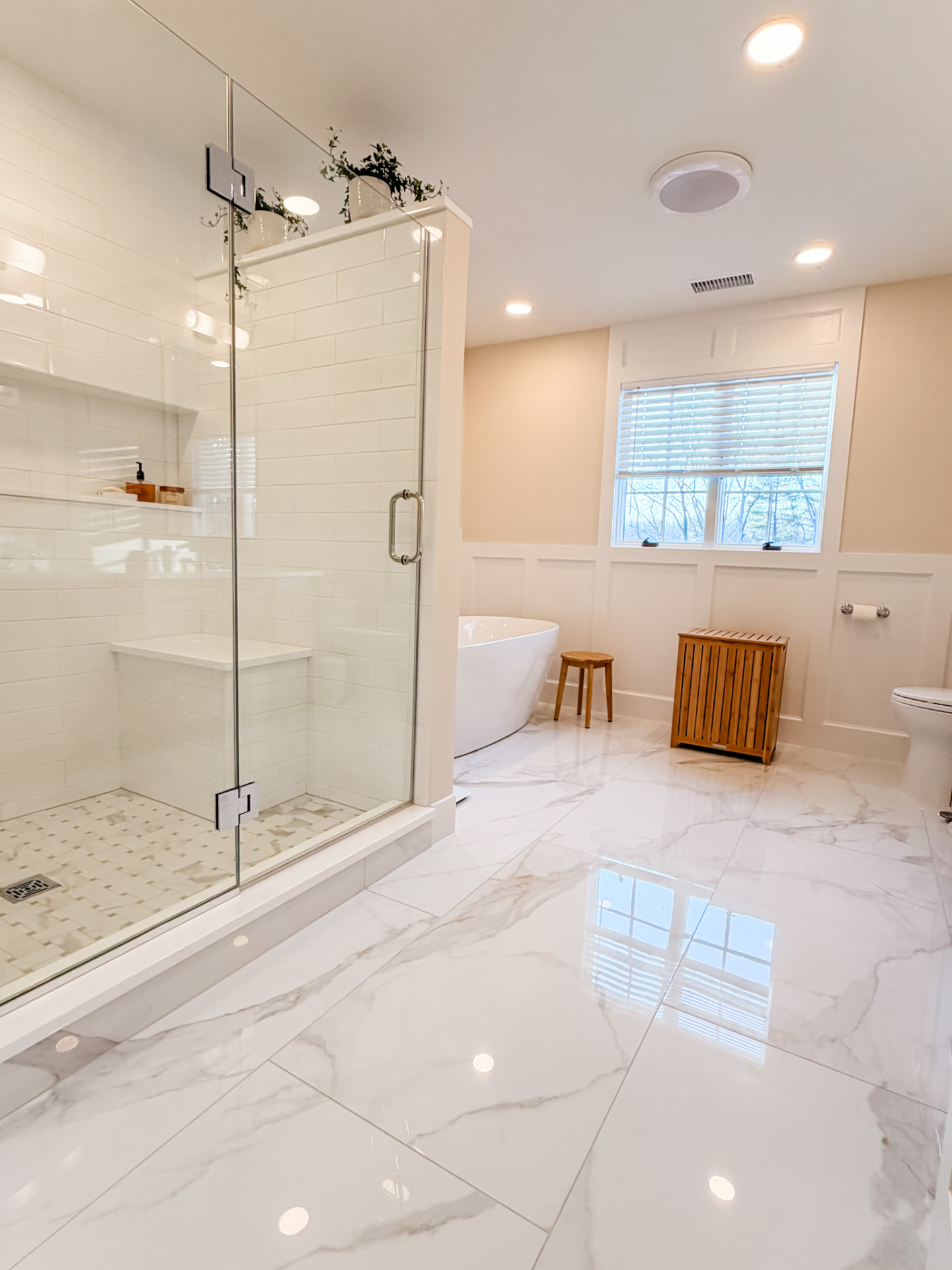 Milan Construction bathroom renovation in New Jersey with a glass walk-in shower, freestanding tub, marble-look tile, and paneled walls
