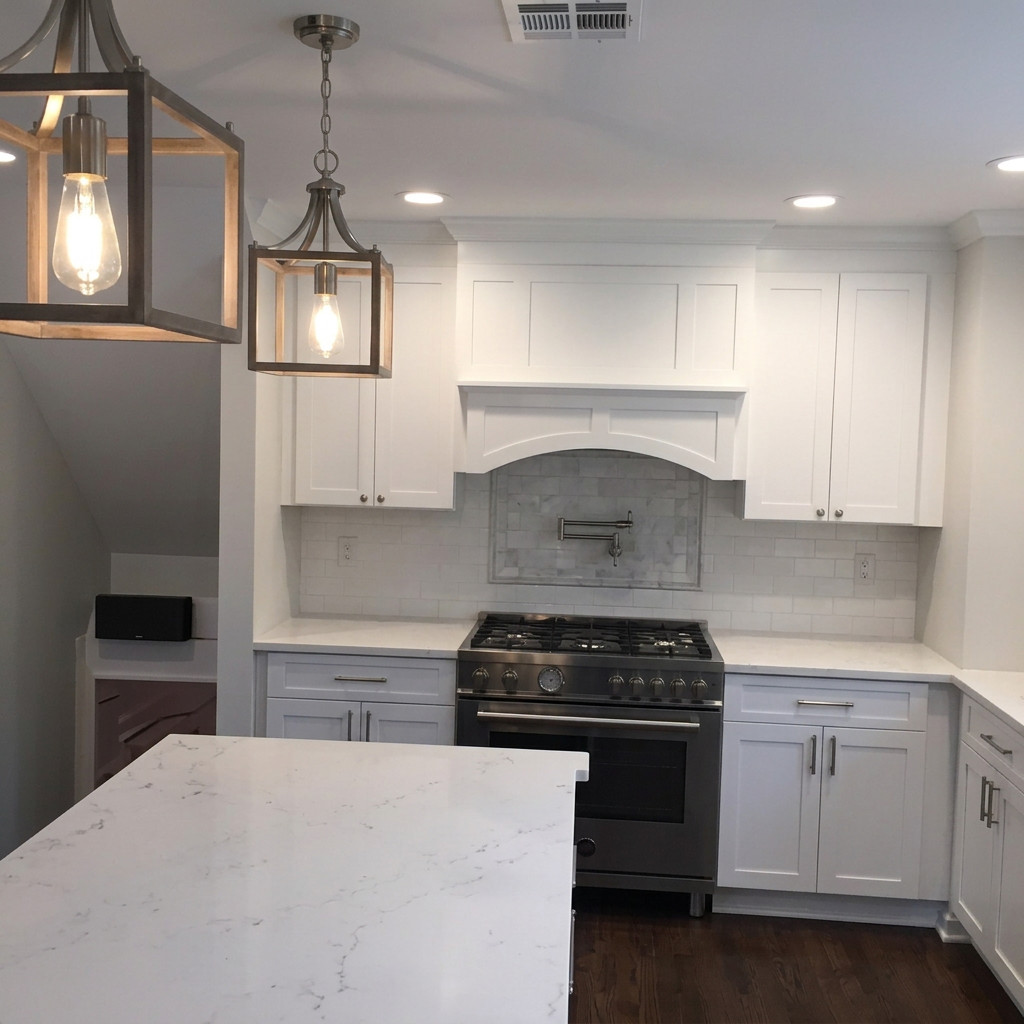 Milan Construction kitchen remodel in New Jersey with white shaker cabinetry, a custom hood surround, tile backsplash, and island pendant lighting